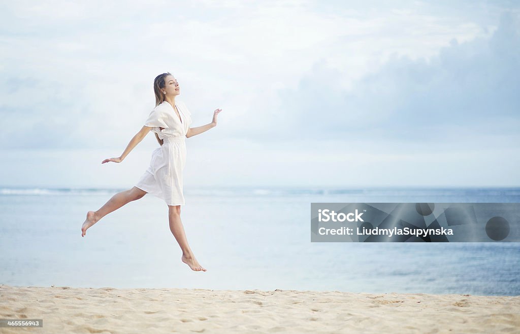 Young woman on the ocean shore in white dress jumping up Beach Stock Photo