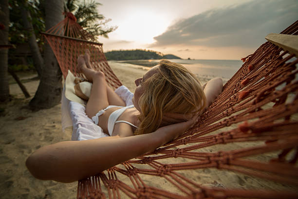 Young woman on a tropical beach in Thailand lying down on a hammock relaxing. Sunset time on the Island. Shot with 5D Mark III.