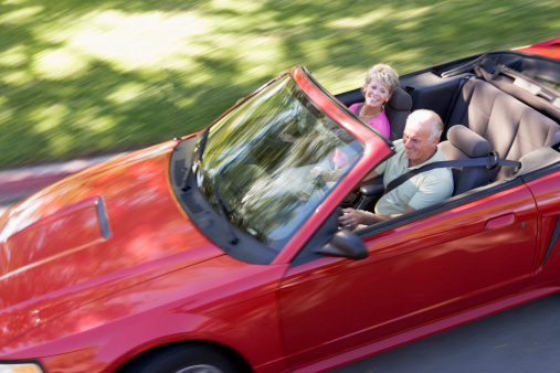 Couple in red convertible car smiling driving down street