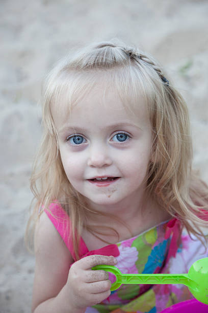 Little Blue Eyed Girl Looking up at camera on beach stock photo