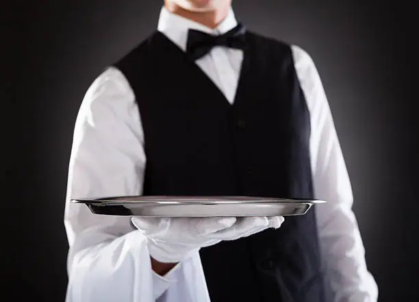 Portrait Of A Male Waiter Holding Tray Over Black Background