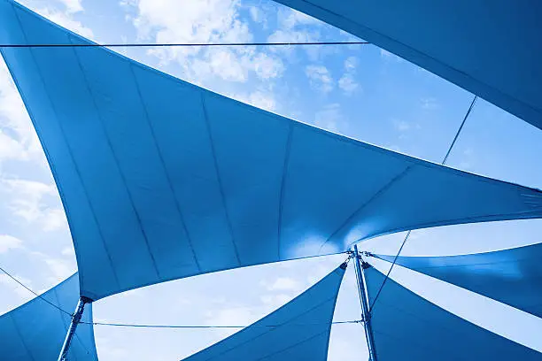 Awnings in sails shape over cloudy sky background. Blue toned photo