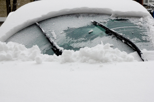 Snow-covered car in the street covered with a thick layer of snow on a winter day.