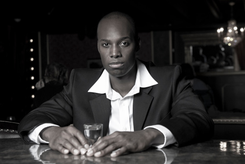 a Black man sitting at a bar in a nightclub; black and white