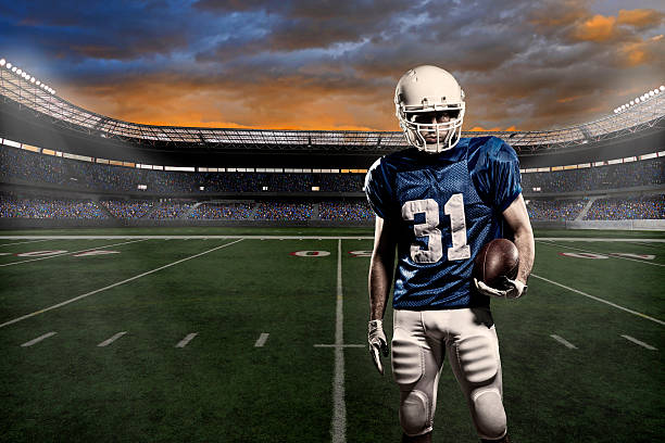 Close-up of a football player in uniform in front of arena Football player with a blue uniform, in a stadium with fans wearing blue uniform. american football player studio stock pictures, royalty-free photos & images