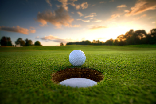 Golf ball about to fall into the cup at sunset