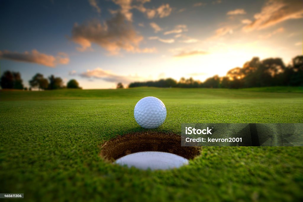 Golf Ball near hole Golf ball about to fall into the cup at sunset Golf Stock Photo