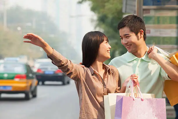Young couple looking at each other with shopping bags hailing a taxicab in Beijing