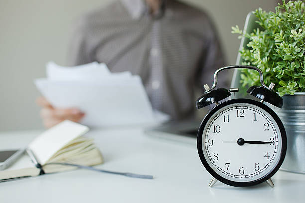 istock Man with papers over table with alarm clock laptop 465632370
