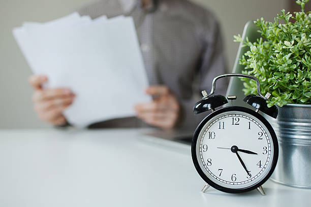istock Man with papers over table with alarm clock laptop 465632376