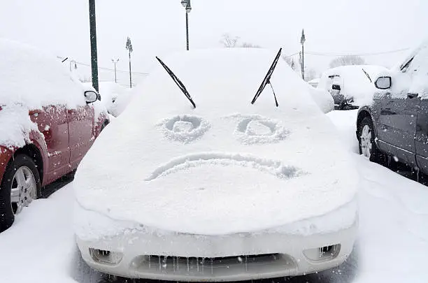 Photo of Sad face emoticon drawn on snow on a car