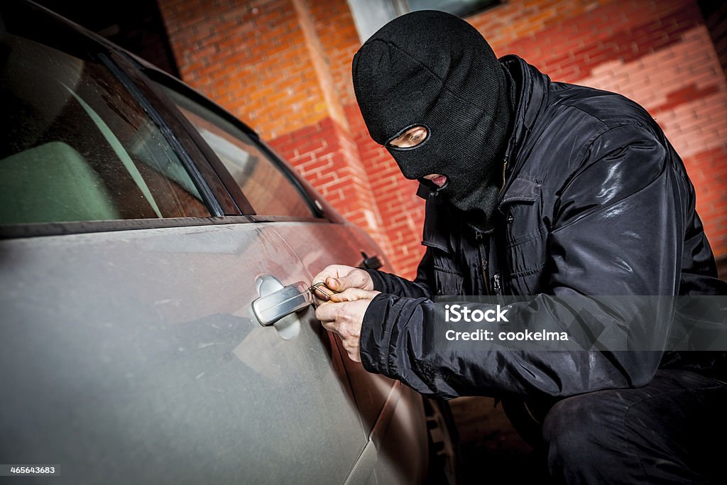 Car thief in a mask. Robber and the car thief in a mask opens the door of the car and hijacks the car. Activity Stock Photo