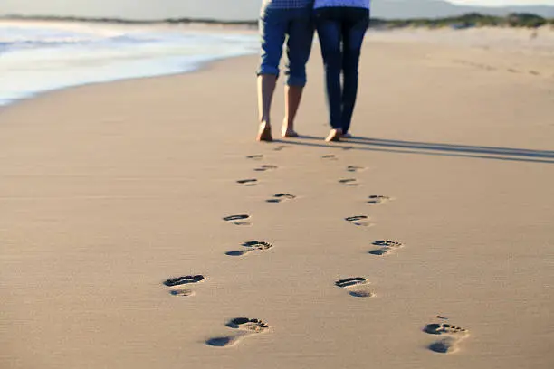 Photo of Couple walking across beach shoreline leaving footprints