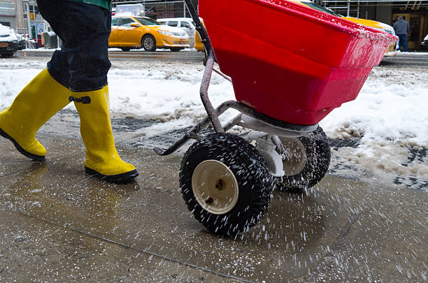 Worker spreading salt on icy sidewalk worker pushing salt spreader on icy New York City sidewalk during snow storm in winter. melting stock pictures, royalty-free photos & images