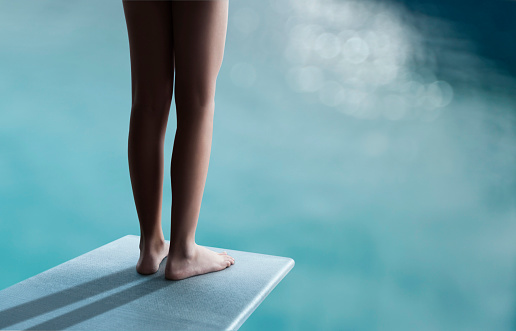 Young boy or girl is standing on a diving board and ready to jump