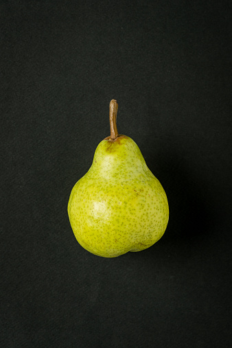 Green pear on black paper background, minimalist still life