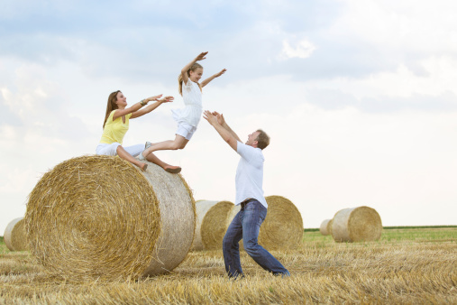 Cheerful little girl jumping from a hay bale into her father's arms.
