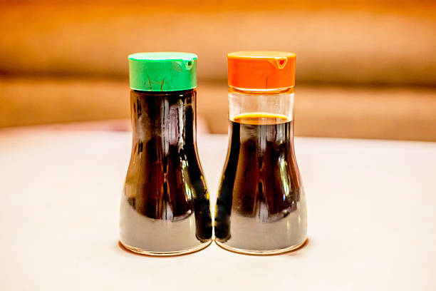 Soy Sauce Bottles Two soy sauce bottles on the table.   One is considered low sodium and has a green top, the other is considered high (or normal) sodium which has a red top. soia sauce stock pictures, royalty-free photos & images