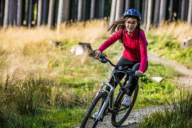Girl wearing protective gear riding bike on forest trail Girl riding bike  mountain biking stock pictures, royalty-free photos & images