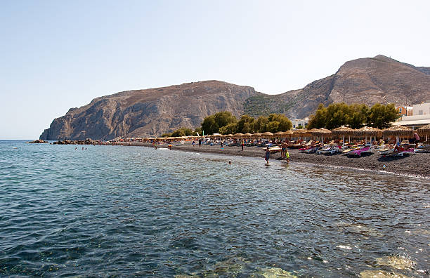 touristen nehmen sie ein sonnenbad auf dem kamari beach. santorin, griechenland. - black sand beach santorini greece stock-fotos und bilder