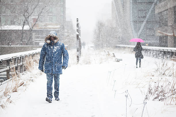 New York City, NY, USA - March 5, 2015: Tourists walk the High Line park during snowstorm. Man in blue parka and a woman in pink umbrella.