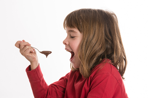 Little girl eating a chocolate custard isolated on white background