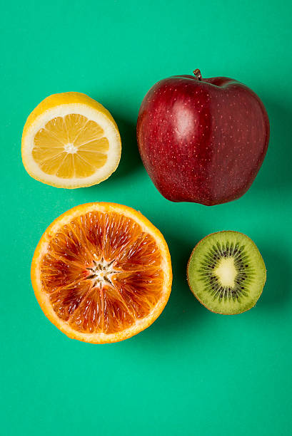 istock Orange, lemon, red apple and kiwi on green paper background 465675924