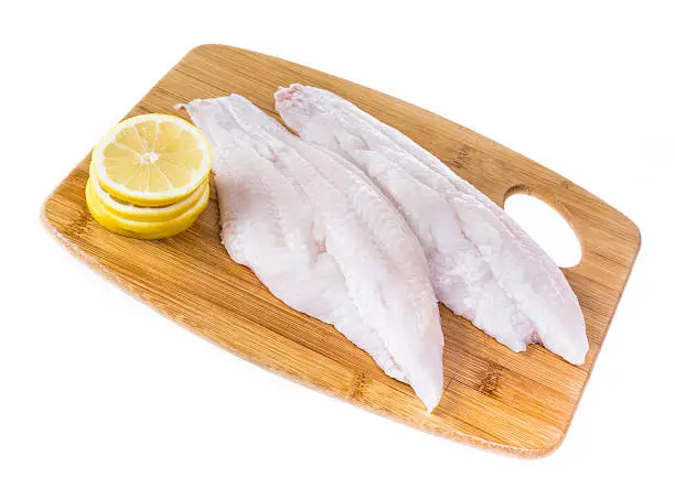 Fresh catfish fillets on a cutting board with lemon and isolated on white.