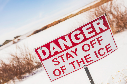 Danger stay off ice sign in front of frozen pond