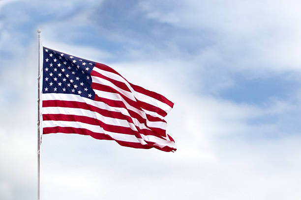 The American flag waving through the wind  Proud American Flag in focus with slightly blurred cloud background. national anthem stock pictures, royalty-free photos & images