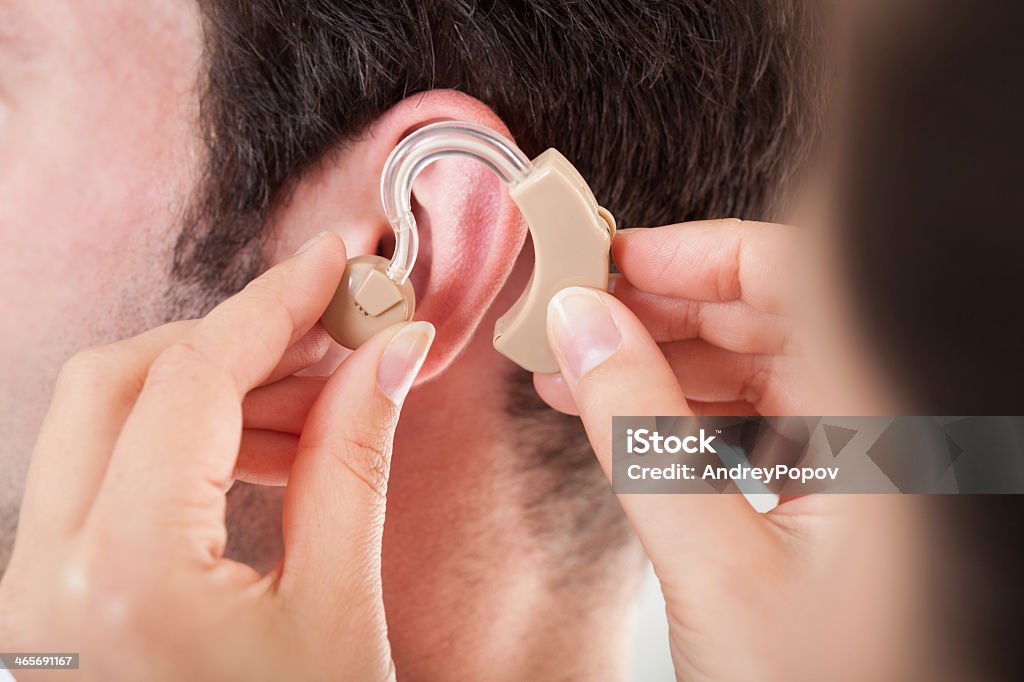 Woman adjusting a hearing aid on a man Close-up Of Hand Helping Young Man To Wear Hearing Aid Hearing Aid Stock Photo