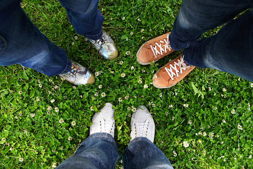 Group of friends standing in a circle on a spring meadow but only their feet in sneakers is visible