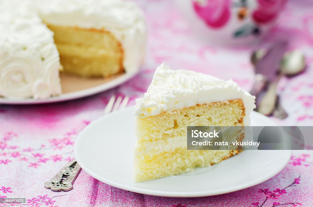 Slice of yellow cake with white frosting on pink table cake with vanilla cream in the form of roses on a pink background. tinting. selective focus Slice of Cake Stock Photo