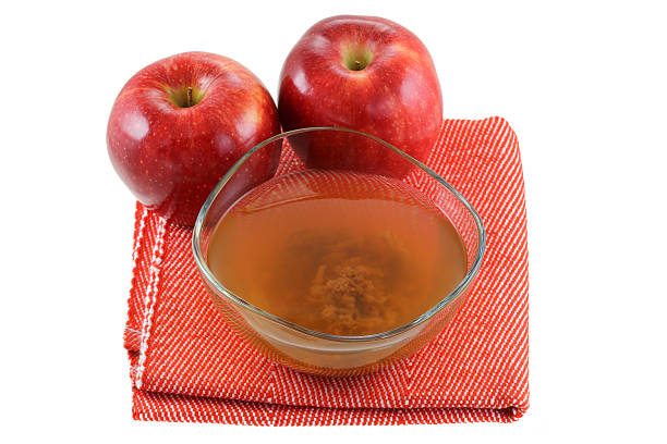 Fresh apples and a bowl of raw and unfiltered organic apple cider vinegar with mother enzymes isolated on white
