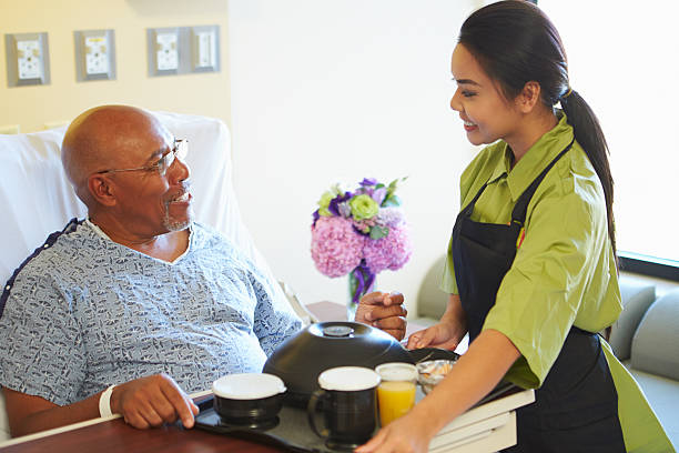 Senior Male Patient Being Served Meal In Hospital Bed Senior Male Patient Being Served Meal On Tray In Hospital Bed serving food and drinks stock pictures, royalty-free photos & images