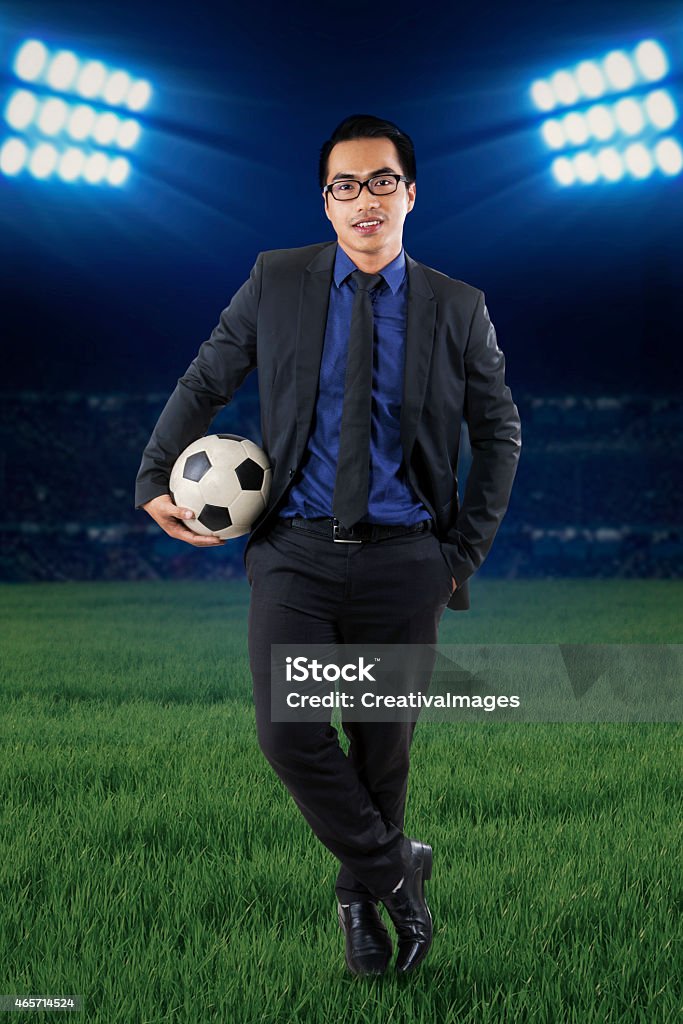 Male manager with football at field Full length of a young businessman standing at field while holding a soccer ball 2015 Stock Photo