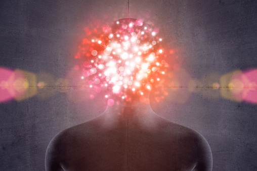 Human upper body and head front view on a dark concrete background: a glowing and vibrant aura of light explosion covers the face, hiding facial features with a network of gleaming round light particles. Pink, red and orange light burst. Horizontal composition, digitally generated image.