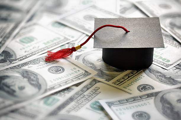 Saving for education Graduation mortar board cap on one hundred dollar bills concept for the cost of a college and university education university stock pictures, royalty-free photos & images