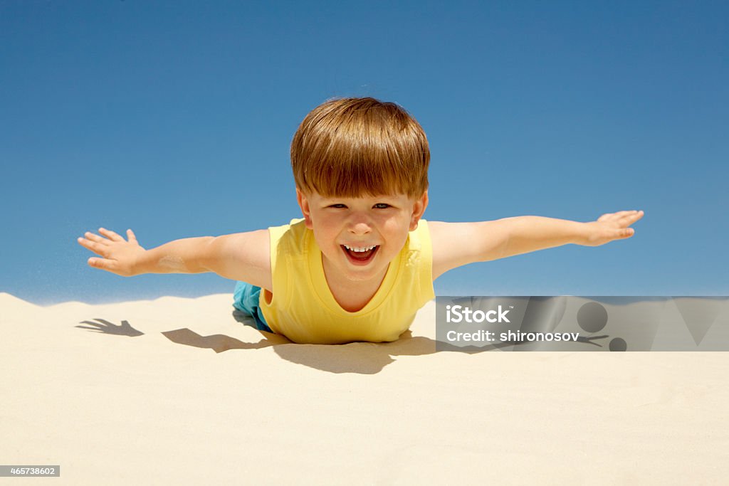 Enjoying sunny day Happy boy lying on sand with outstretched arms and looking at camera on beach 2015 Stock Photo
