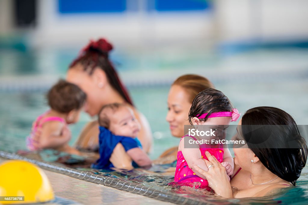 Group of mothers swimming with their babies A group of mothers introducing their babies to the water in an indoor pool at a health club Learning Stock Photo