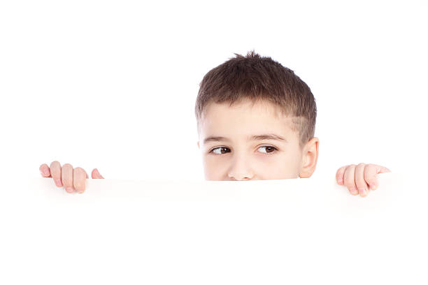 Young boy hiding behind a billboard and making face stock photo