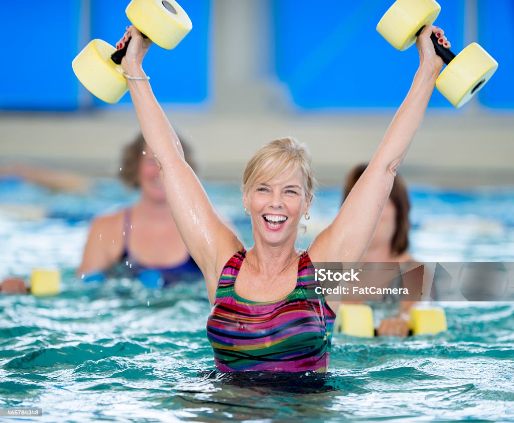 Excited Seniors Water Aerobics A group of seniors practicing water aerobics in an indoor pool, with one team member very excited 2015 Stock Photo