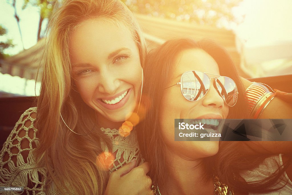 Close-up of two cheerful friends having fun at a cafe Closeup of two cheerful friends having fun at a cafe. Shallow DOF. Shallow contrast and lens flare due to the sunlight from the back side.Developed from RAW; retouched with special care and attention; Small amount of grain added for best final impression; Adobe RGB color profile; Ready made for print and web use. Sunset Stock Photo