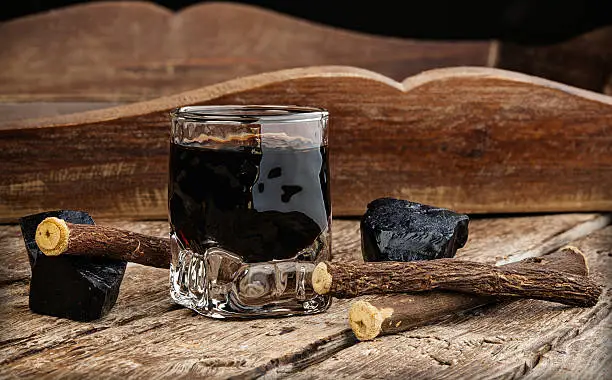 Licorice liqueur with pure blocks and roots on wooden table.