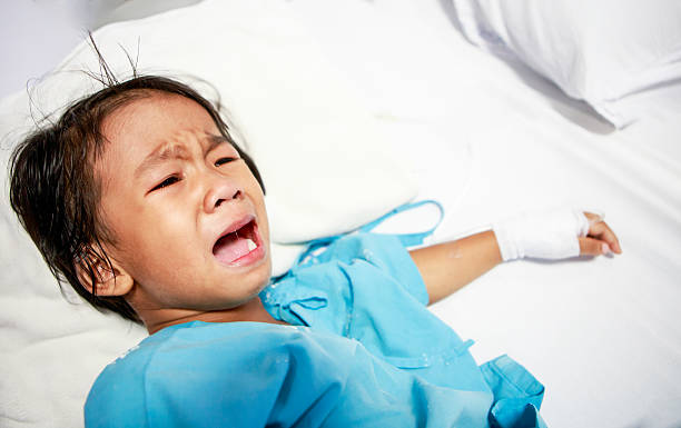 Sick little girl crying in hospital bed stock photo