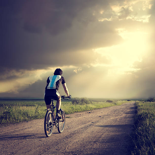 Epic Photo of Cyclist on the Country Road. Rear View. Dramatic Sky Background. Hope for Better Future Concept. Instagram Styled Toned Photo. Copyspace.