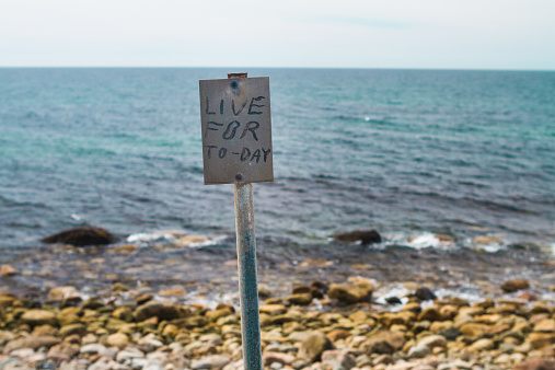 The phrase Live for Today is printed on the inspirational signpost on the shore with ocean background