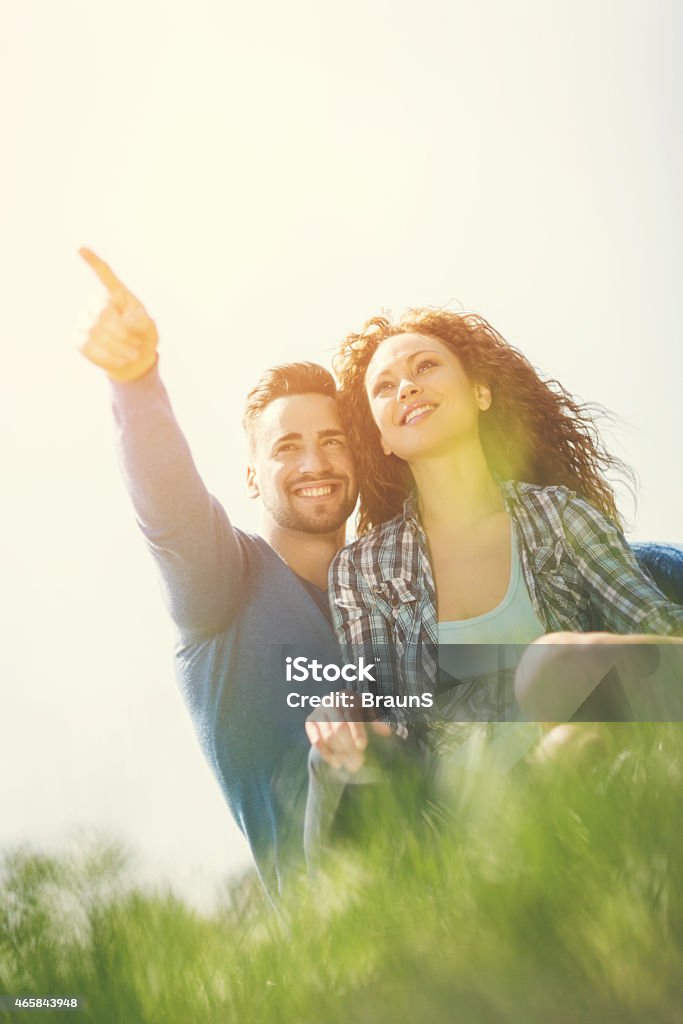 Can you see that? Low angle view of young happy couple enjoying in the park. Man is pointing at something. 2015 Stock Photo