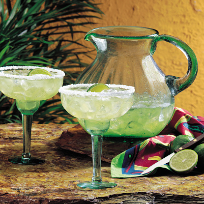 2 margarita glasses with a pitcher of margaritas on a table with a Mexican style napkin