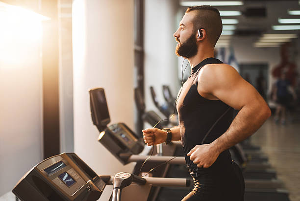 Side view of a young athlete running on treadmill. Young muscular man jogging on treadmill in a gym. treadmill stock pictures, royalty-free photos & images